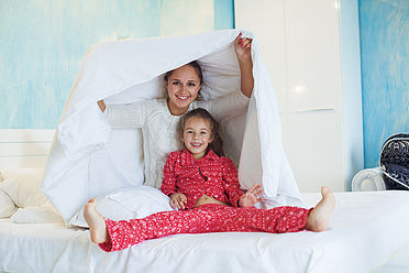 Mom with her 6 years old little daughter dressed in winter pajamas are relaxing and playing in the bed at the weekend together, lazy morning, warm and cozy scene.